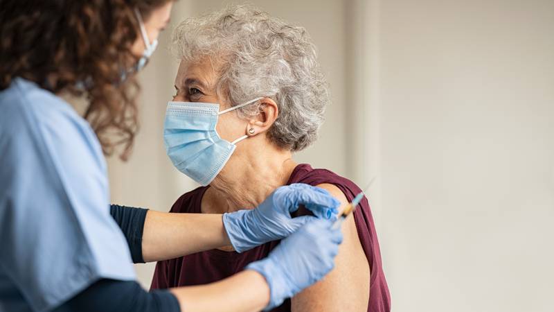 Doctor giving injection to senior woman at hospital.