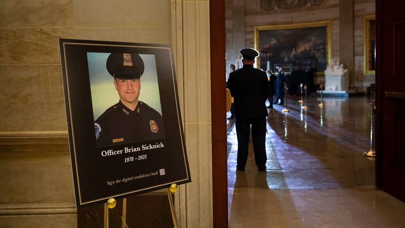 FILE PHOTO: In this Feb. 2, 2021, file photo a placard is displayed with an image of the late U.S. Capitol Police officer Brian Sicknick on it as people wait for an urn with his cremated remains to be carried into the U.S. Capitol to lie in honor in the Capitol Rotunda in Washington. Two people have been charged with assaulting Sicknick.