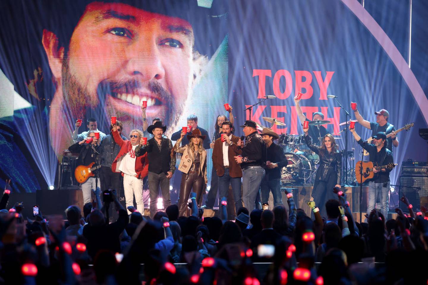 A group of performers hold up red Solo cups to honor Toby Keith.