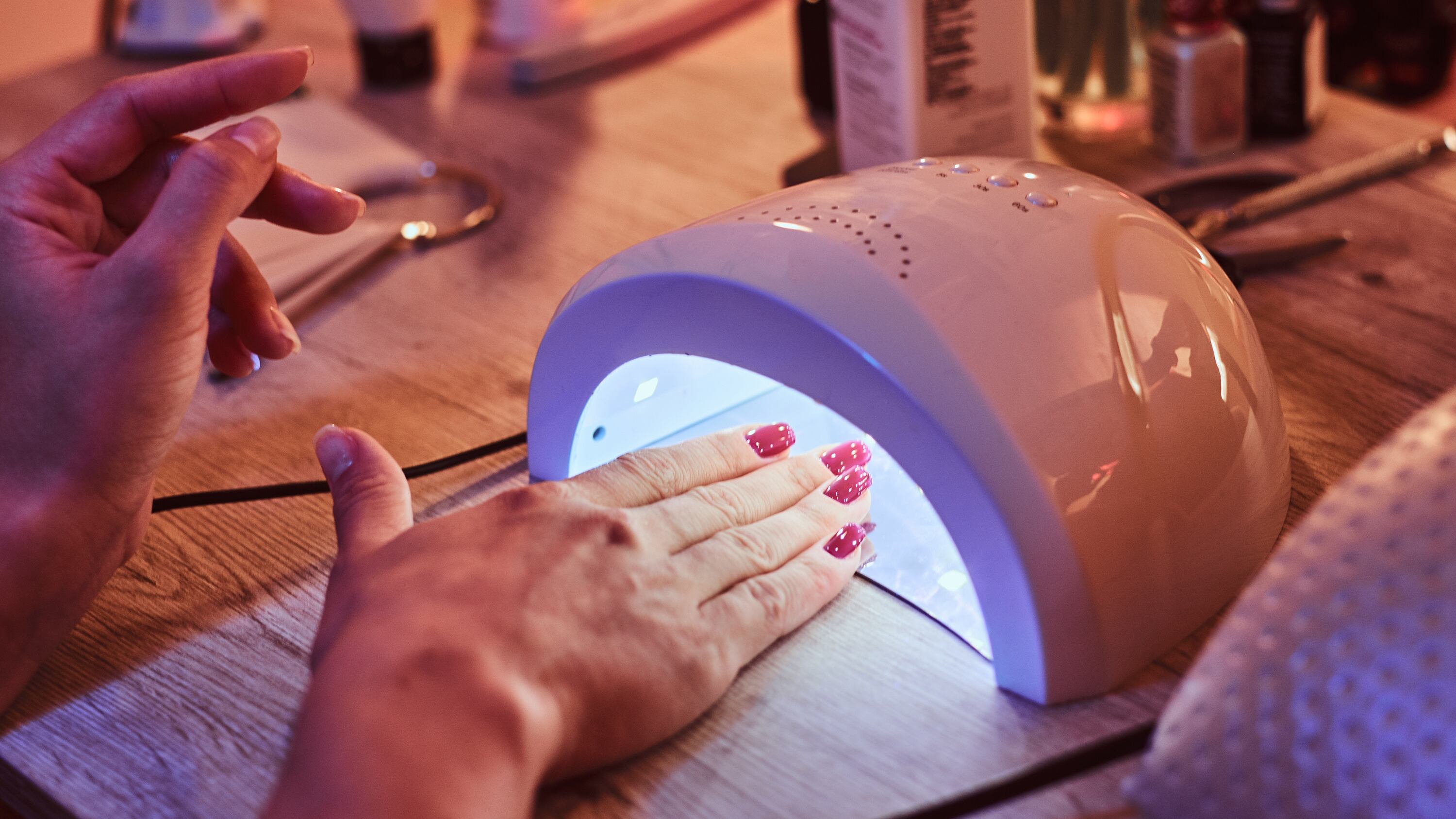 Client with red varnish at manicure salon carefully waiting when her nails become dry in UV light