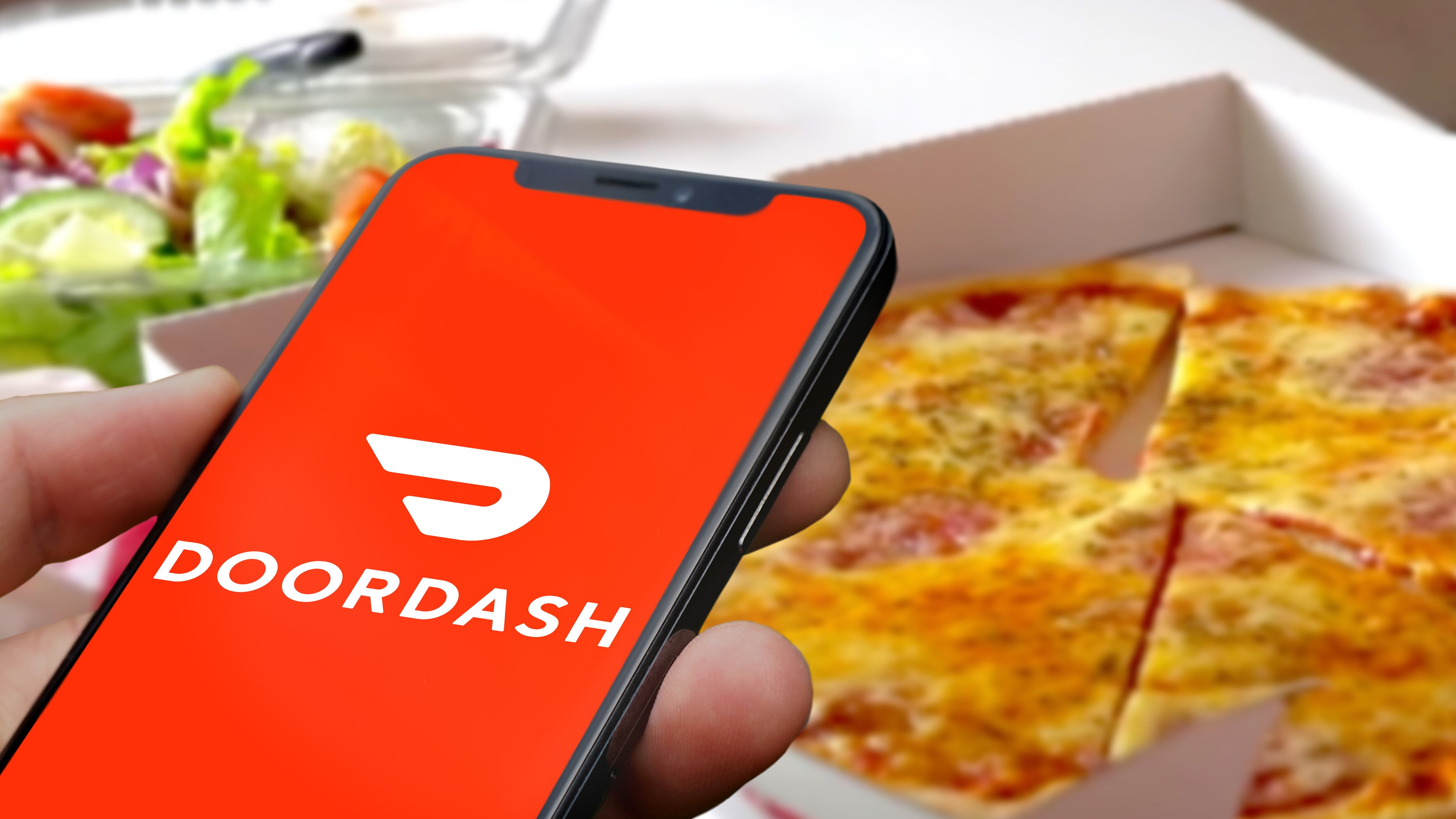 DoorDash on a smartphone with pizza and a salad in the background.